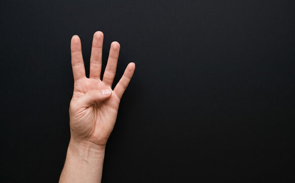 Hand showing four fingers gesture on dark background representing counting and communication