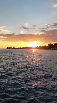 Dynamic vertical clip of golden sunset light glittering across active sea waves near a silhouetted coastal town in Biak, Papua, Indonesia, ideal for social media reels and video transitions.