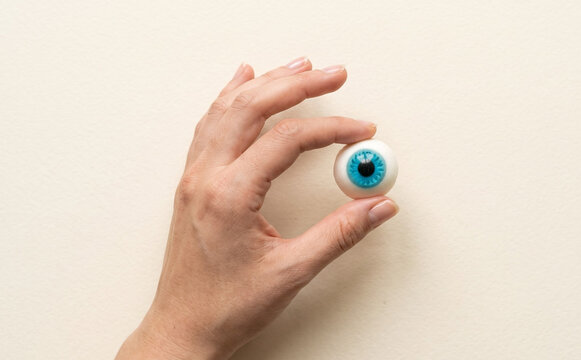 Hand holding a toy blue plastic eyeball representing spooky Halloween concepts and surreal vision themes