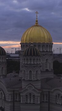 An aerial panning shot shows the golden domes and Byzantine revival architecture of the Nativity of Christ Cathedral in Riga, Latvia, at sunset.