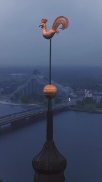 Aerial view showing the golden rooster weather vane of Riga Cathedral spire with the Daugava River and cityscape at dusk, Latvia.