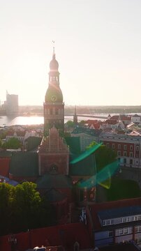 Aerial view showing the historic Riga Cathedral and Old Town architecture with the Daugava river bathed in warm sunset light in Latvia.