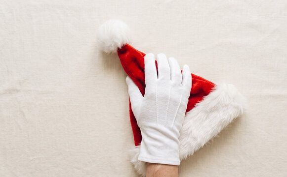 White gloved hand holding a Santa Claus hat on a neutral background for holiday design concepts