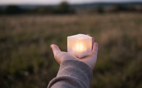 A hand holding a glowing cube light in an outdoor field at dusk representing hope and magic
