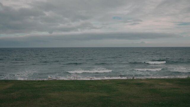 A grassy field with a gray sky and sea in the background