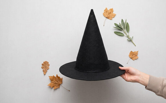 Black witch hat held by a hand surrounded by autumn leaves for Halloween concepts