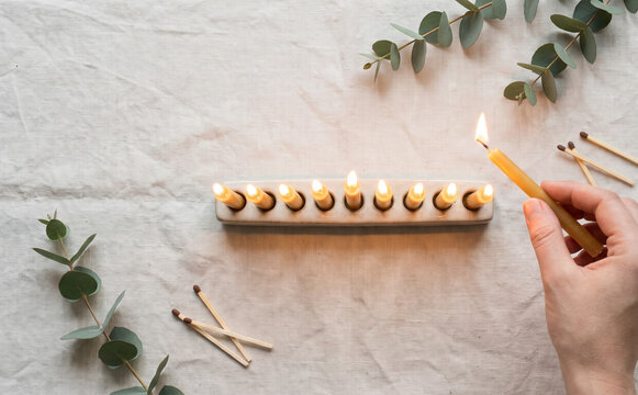 Lighting a Hanukkah menorah with yellow beeswax candles and eucalyptus branches on linen