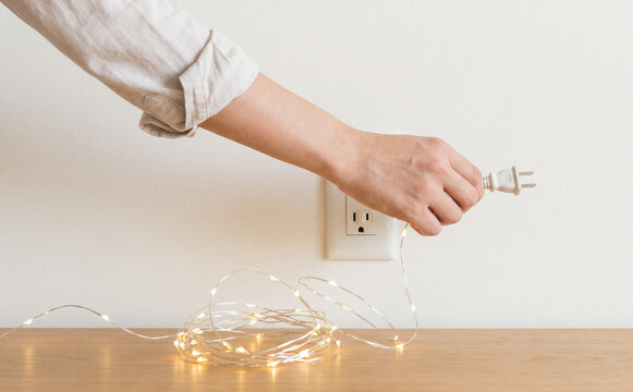 Woman unplugging fairy lights from wall outlet on wooden desk in minimalist interior