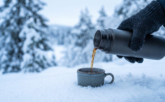 Hot coffee being poured from a thermos into a mug in a snowy winter forest landscape