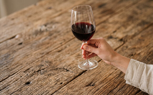Woman holding a glass of red wine on a rustic wooden table for wine tasting concept