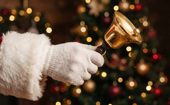 Santa Claus ringing a golden hand bell in front of a Christmas tree with bokeh lights for holiday greeting concepts
