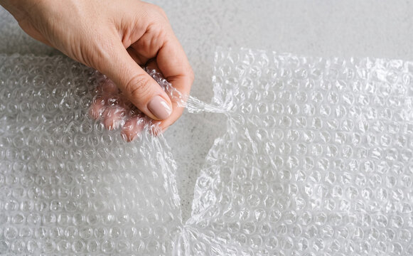 Hands tearing plastic bubble wrap packaging material for shipping protection and stress relief