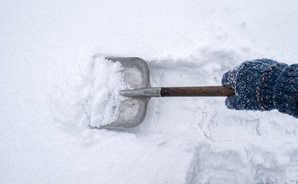 Person shoveling fresh white snow with a metal shovel wearing a warm winter glove