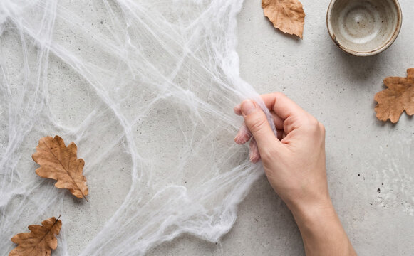 Decorating a concrete tabletop with fake spider webs and autumn oak leaves for Halloween