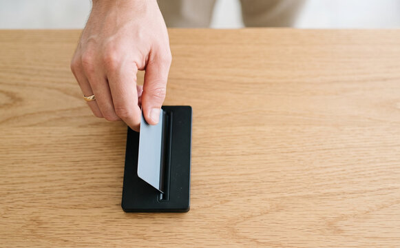 Man swiping credit card through a card reader terminal on a wooden desk to make a secure payment