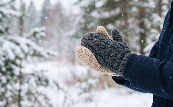 Person wearing warm knitted mittens outdoors in a snowy winter forest for seasonal concept