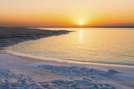 Dead Sea Jordan sunset with orange glow, calm water reflection, palm silhouettes, peaceful travel mood, nature beauty, climate and water scarcity concept