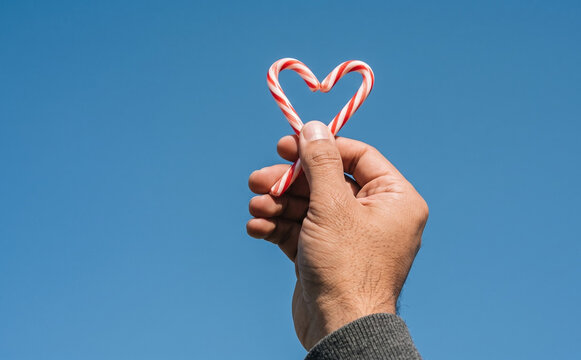 Man holding two candy canes shaped like a heart against clear blue sky representing love and Christmas