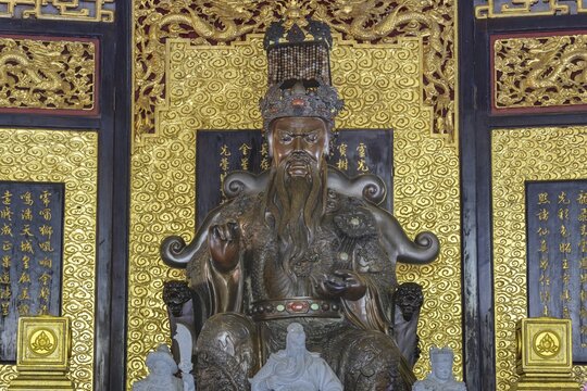 A deity seated majestically on a throne, Shou Xing (also known as Shou Lao or Nanji Xianweng), the god of longevity, carved from dark wood with gold inlays, surrounded by dragon motifs and cloud patterns, symbolises wisdom and long life in Chinese-Daoist culture, Chee Chin Khor Temple, Bangkok, Thailand