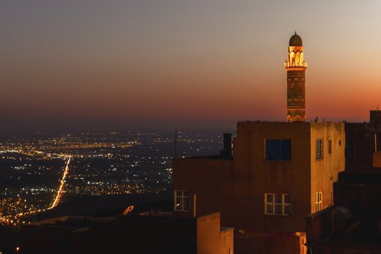 Illuminated mosque minaret above Mardin old town with glowing city lights and Mesopotamian plains at sunset. Great Mosque of Mardin Ulu Camii Minaret