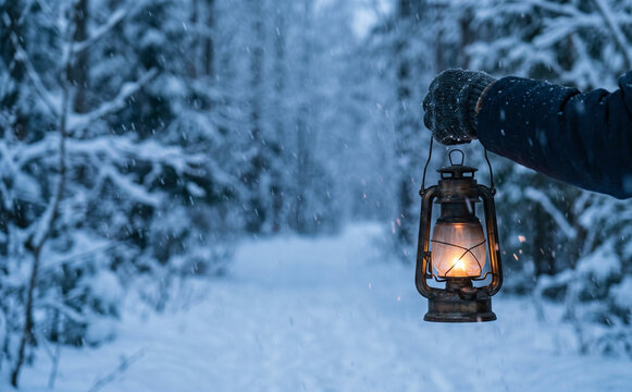 Person holding vintage lantern in snowy winter forest walking outdoors at night concept for cozy holiday adventure