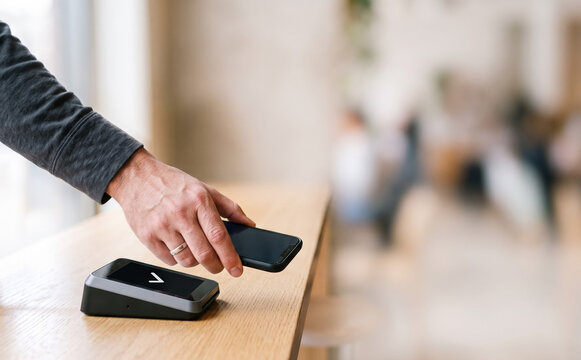 Contactless mobile payment with smartphone at terminal in cafe by young caucasian man