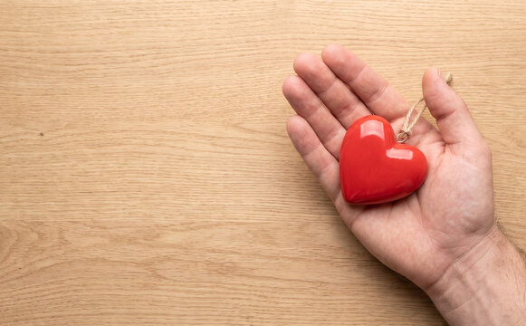 Male adult hand holding red heart on wooden background for love and health charity concept