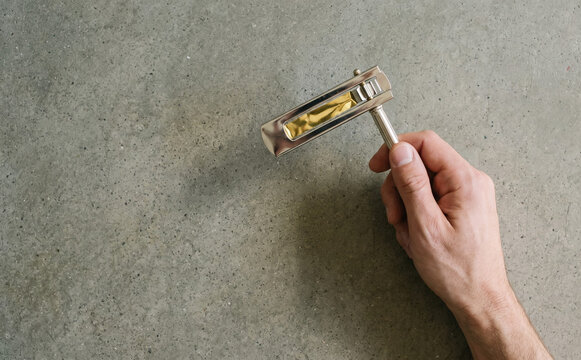 A person holding a traditional metal Purim noisemaker ratchet over a neutral concrete background