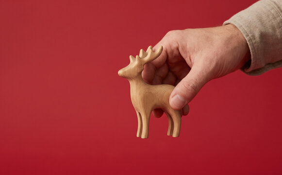 A hand holding a wooden deer figurine on a red background for Christmas decor concepts