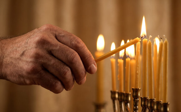Elderly man lighting Hanukkah menorah candles with warm festive glow representing tradition and faith