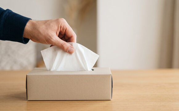 Man pulling white tissue paper from cardboard box on wooden table representing hygiene and health care
