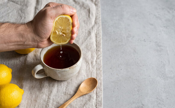Man squeezing a fresh yellow lemon into a cup of black tea with a wooden spoon for a healthy morning routine