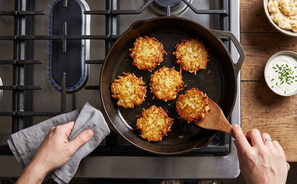 Cooking delicious potato latkes in a cast iron skillet on a stovetop with sour cream