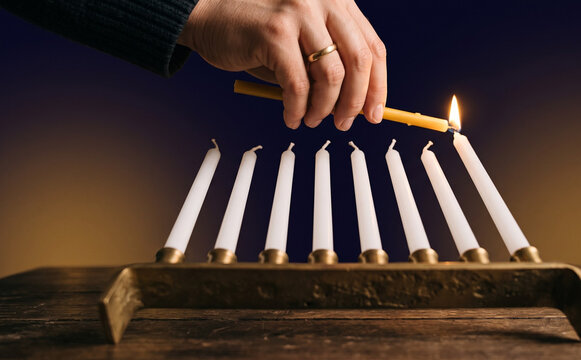 Person lighting a menorah candle for Hanukkah celebration holiday tradition