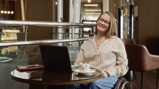Portrait of Caucasian woman with disability in wheelchair typing on laptop, looking at camera and smiling. Footage is ideal for corporate diversity and inclusion marketing
