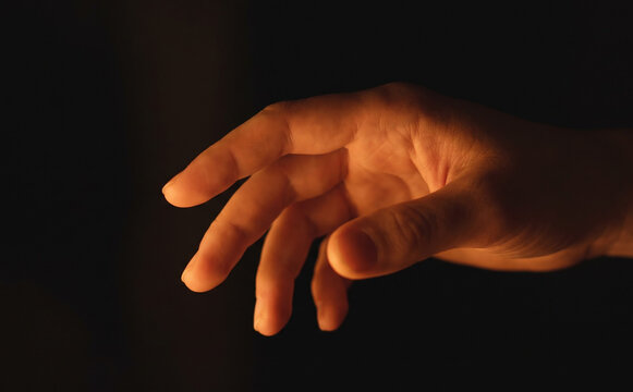 Human hand reaching out in the dark illuminated by warm light representing hope and connection