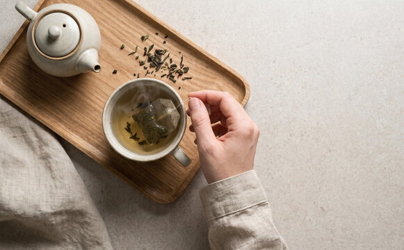 Woman making hot green tea with teabag and teapot on a wooden tray