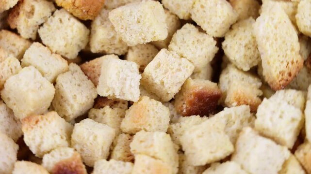 Close-up of golden bread croutons rotating. Crunchy toasted bread cubes texture. Dry wheat crouton food background for salad, soup and snack concept