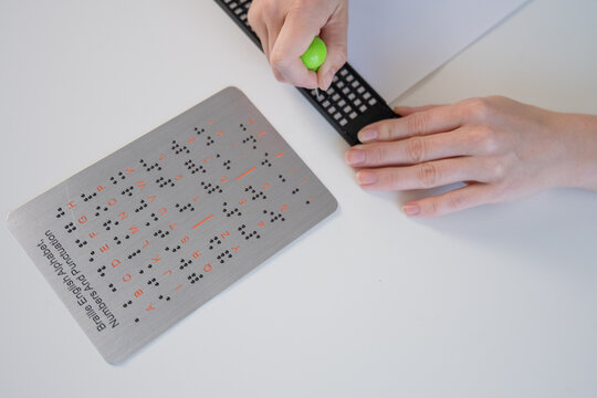 A blind woman writes in Braille using a stencil on a piece of paper. 