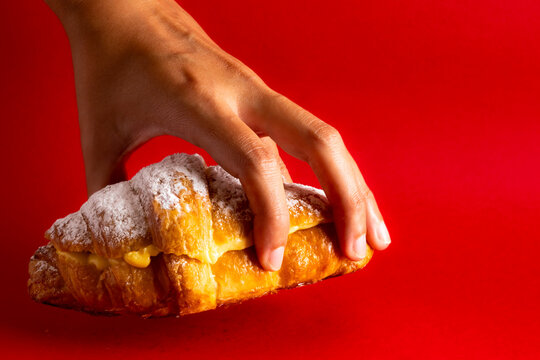 Hand lifting a fresh custard croissant over red background