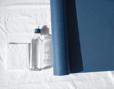 Blue yoga mat and reusable water bottle on white textured surface