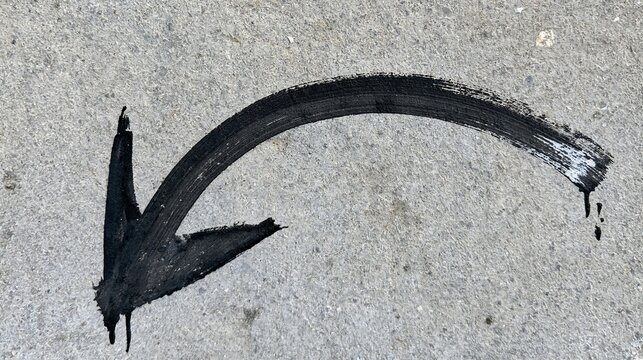 Arched black marker arrow pointing down painted on a textured concrete pavement surface. Ideal for navigation, wayfinding, and directional concepts.