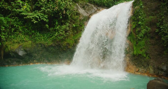 Turquoise river and waterfall rushing between large boulders surrounded by rainforest in Costa Rica