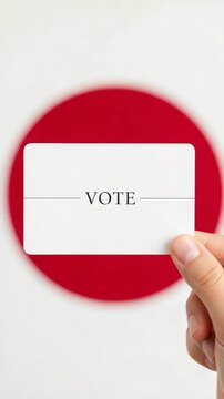 Hand holding a white voting card with the word VOTE printed on it against a red circular background representing election concepts