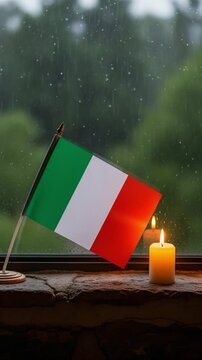 Italian flag and burning candle by a rainy window, symbolizing remembrance, hope, and patriotism in Italy