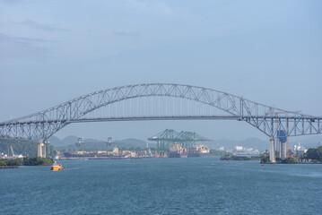 Fototapeta premium Scenic panorama of the Bridge of the Americas viewed from the ocean, with container ships and port infrastructure visible in the distance.