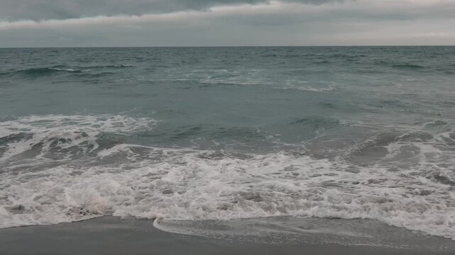 Intermittent waves breaking on a gray sandy beach beneath a gray sky
