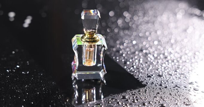 Stylish presentation of perfume in bottle on black background with water drops, closeup. Camera moving right
