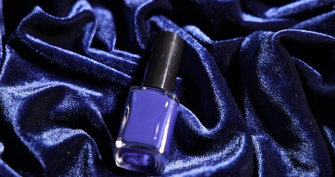 Nail polish in bottle on sparkly blue fabric, closeup. Camera moving forward