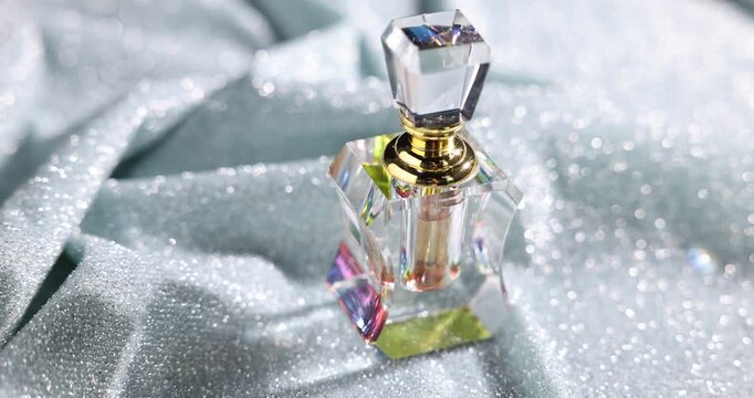 Aromatic perfume in bottle on sparkly light blue fabric, closeup. Camera moving right
